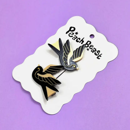 Set of two black and gold sparrow hair clips on a white card against a purple background.
