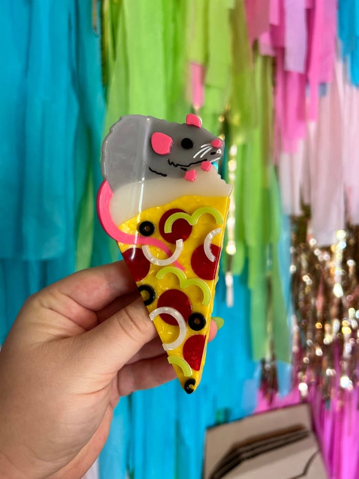 Hand holding the pizza rat hair claw against a colorful background.