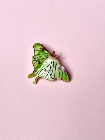 Green Luna Moth hair clip on a pink background.
