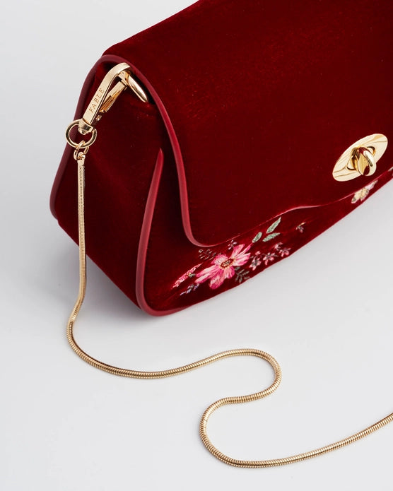 Close up of gold chain attached with a clip to the red velvet purse against a white background.