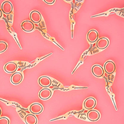 Multiple gold stork scissor barrettes against a pink background.