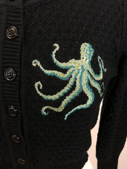 Close up of one of the octopus on the cardigan. Octopus is various shades of green on a black cardigan.