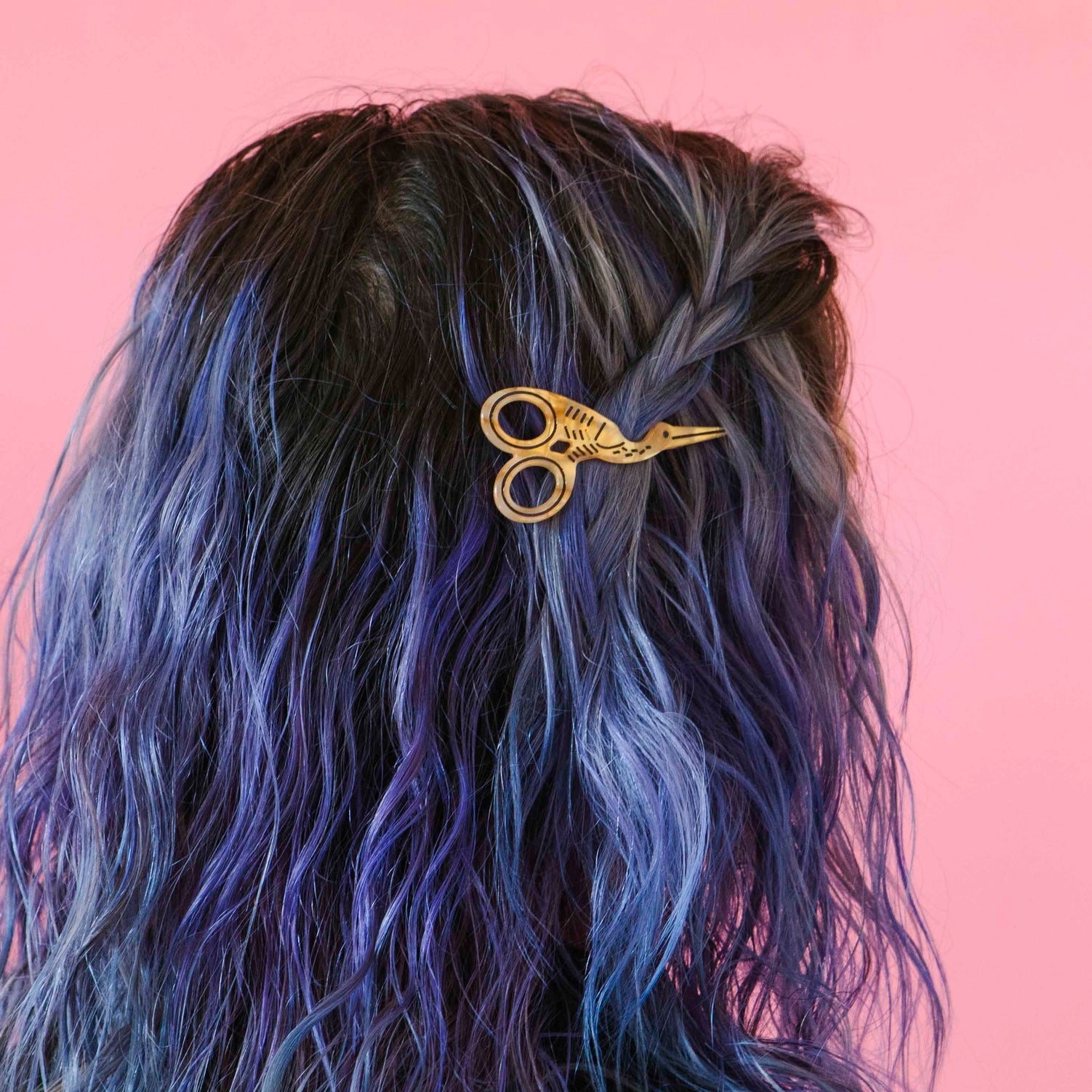 Multi-color haired model wearing gold stork scissor hair barrette against a pink background.