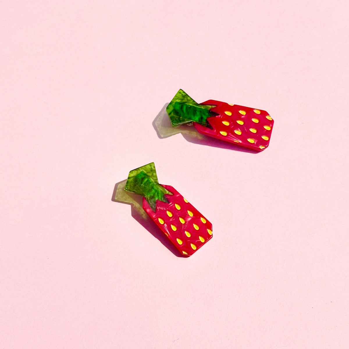 Red strawberry candy hair clips with green tops against a pink background.