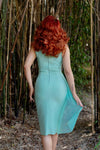 Model with bright red hair showcasing the back of the dress against a bamboo forest background