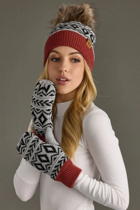 Woman wearing a red knit hat with a pom-pom and patterned mittens against a gray background.