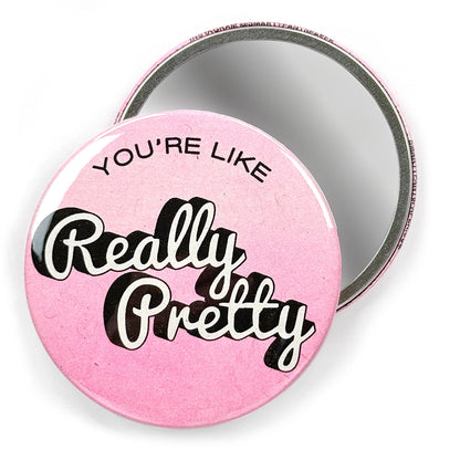 Mirror with "You're Like Really Pretty" in white and black lettering on pink with a second mirror behind it facing with mirror out against a white background.