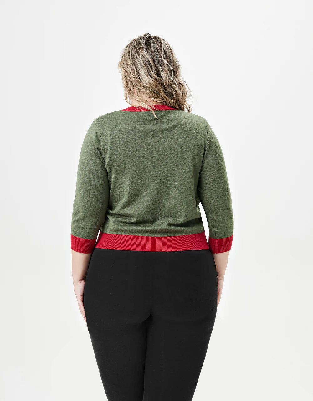 A plus-sized woman with wavy blonde hair is photographed from behind, wearing a light olive-green cardigan with bright red trim along the neckline, cuffs, and waistband. The cardigan has three-quarter-length sleeves and is paired with black pants. The back of the cardigan is plain, without any embellishments, and the photo is set against a white background.