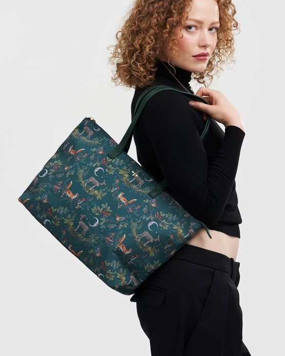 Female model with tote bag on their side with arm up by handle against a white background.