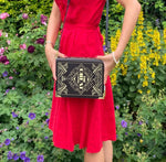 Model wearing a red dress showcases purse at her side against a forestry background