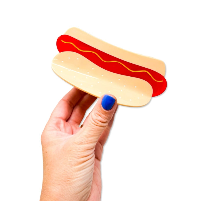 Hand holding hot dog hair claw against a white background.