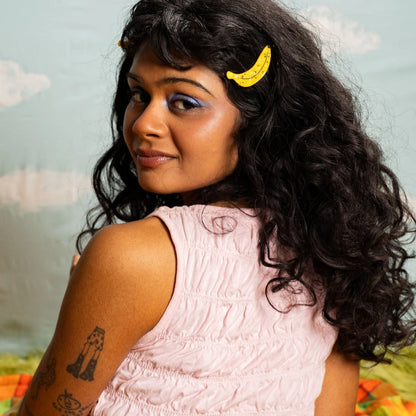 Brunette model wearing a ripe yellow banana hair clip against a light background.