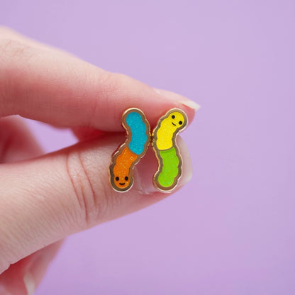 Gummy worm earrings held by a hand against a pink background.