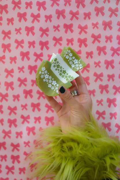 Hand holding the hair claw against a pink background with red bows.