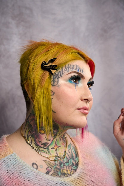 Yellow haired model with tattoos wearing hair clip against a light background.