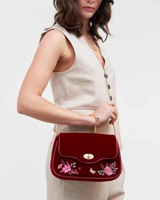 Front of red velvet purse with long gold chain on a female model with brown hair against a white background.
