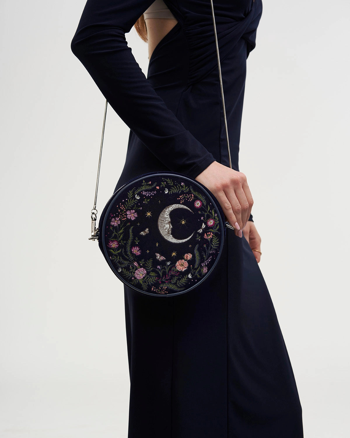 Model in a dark dress wearing the purse at their side against a white background.