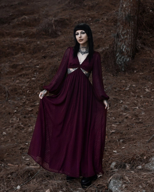 Woman in a long burgundy dress standing in a forest setting.