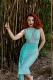 Model with bright red hair showcasing front of the dress in a dramatic pose against a bamboo forest background