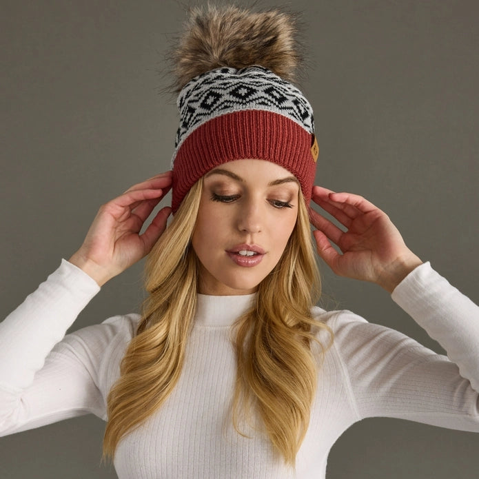 Woman wearing a patterned knit beanie with a pom-pom on a plain background.