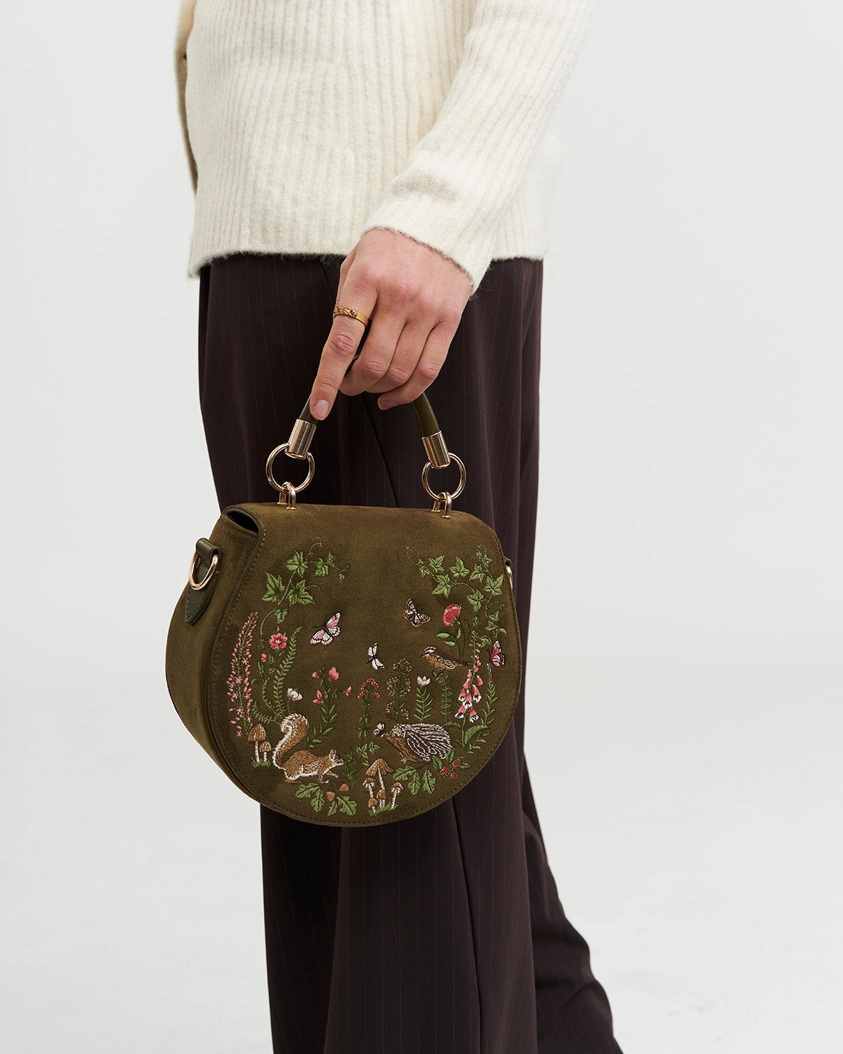 Model holding green saddle bag by short handle against a white background.