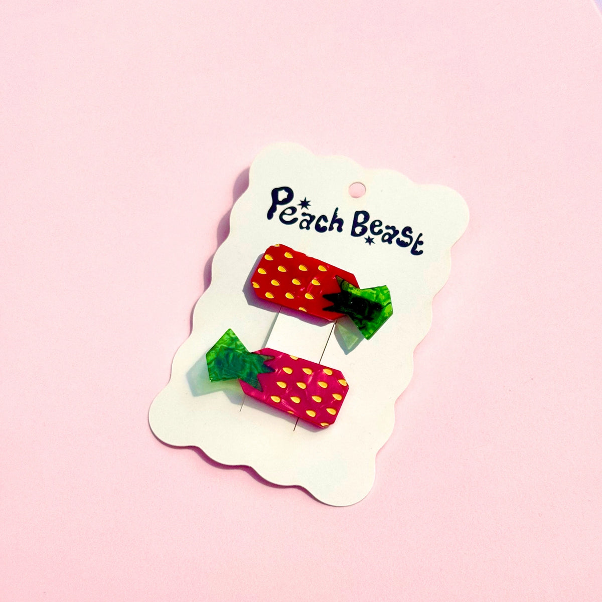 Red strawberry hair clips on a white "Peach Beast" hang tag against a pink background.