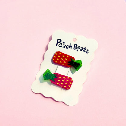 Red strawberry hair clips on a white "Peach Beast" hang tag against a pink background.