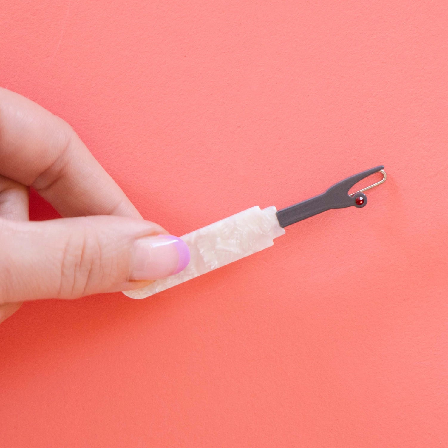 Model hand holding seam ripper hair barrette against a pink background.