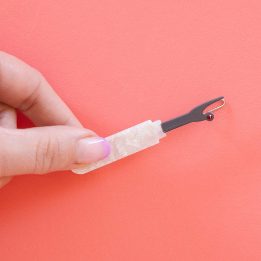 Model hand holding seam ripper hair barrette against a pink background.
