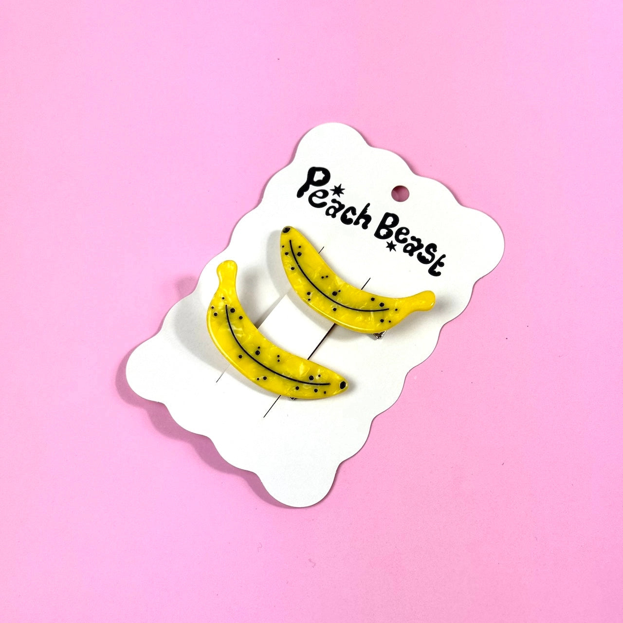 Two ripe banana clips on a white hang card against a pink background.