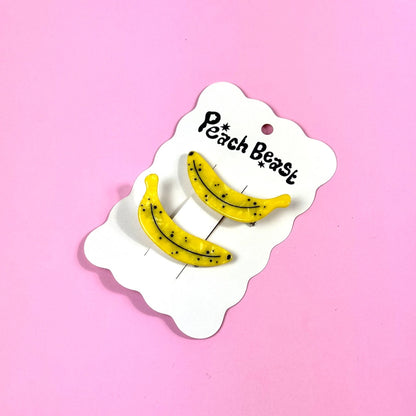 Two ripe banana clips on a white hang card against a pink background.