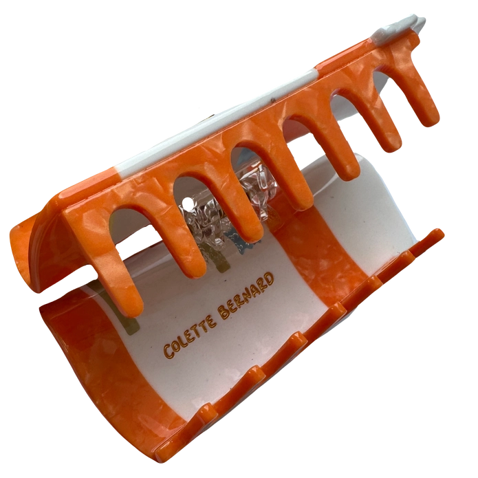 Orange teeth of hair claw opened with 'Colette Bernard' branding on the inside against a blank background.