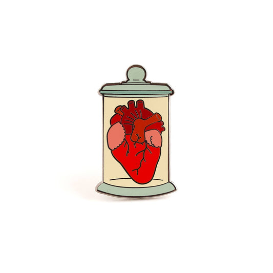 An anatomically correct red heart inside of a cylindrical jar that has a slight yellow background. Pin is shown against a white background