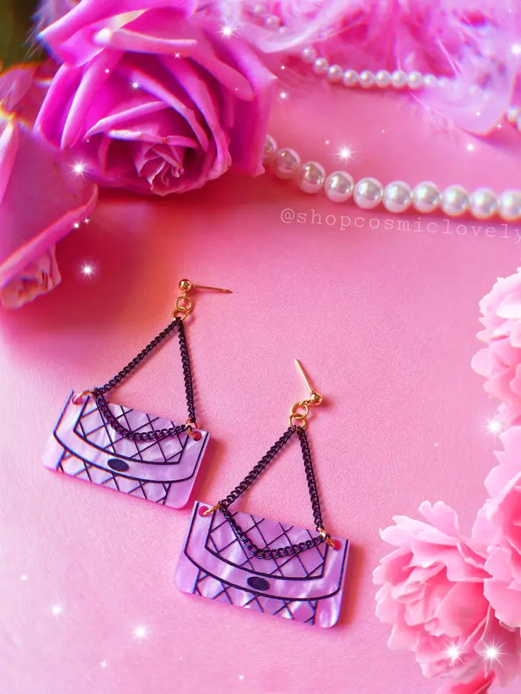 Earrings against a pink background with floral and feather accents