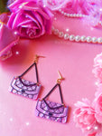 Earrings against a pink background with floral and feather accents