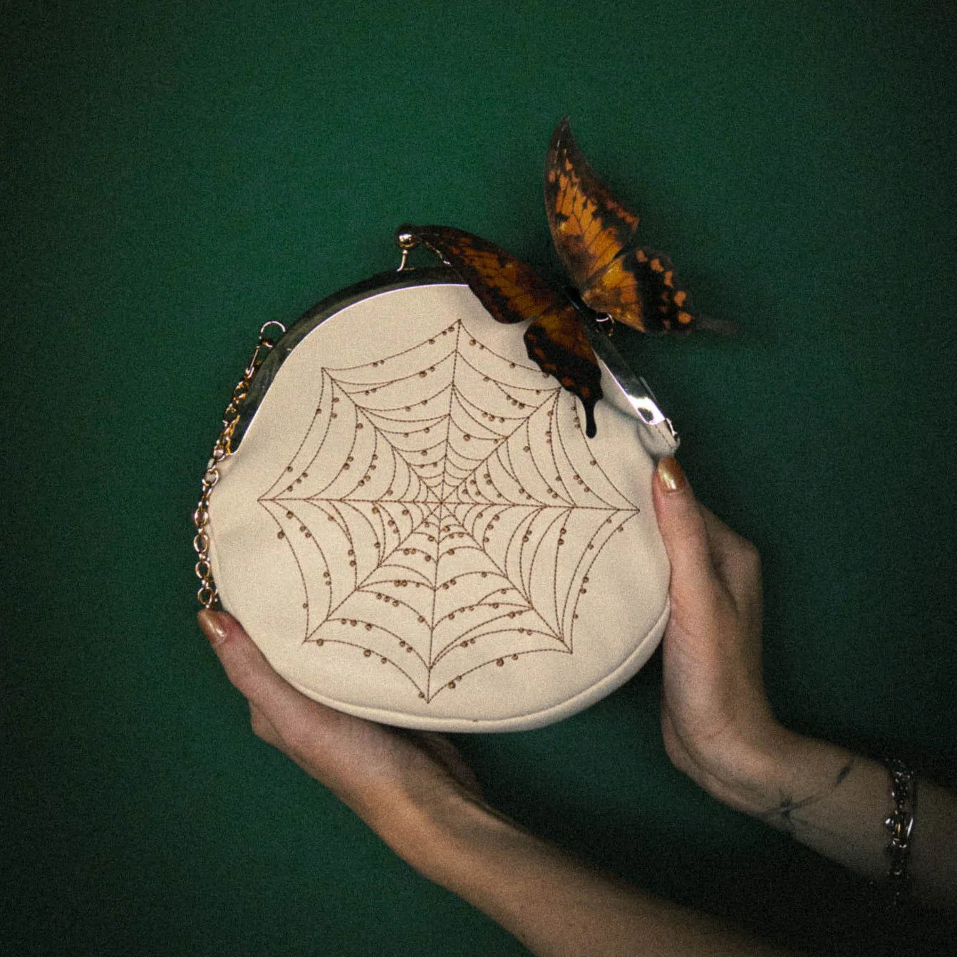 Purse being held against a dark green background with a butterfly on the top right of it