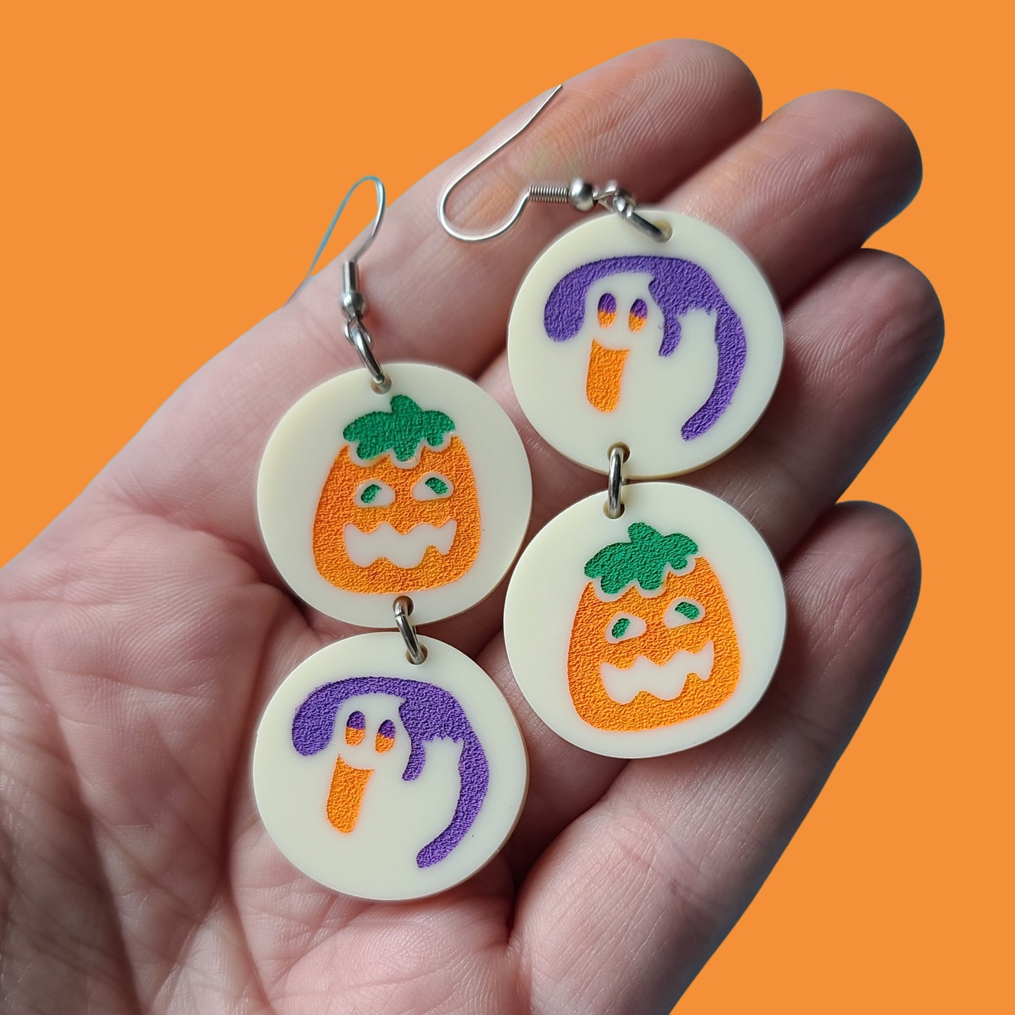 Hand holding earrings against orange background