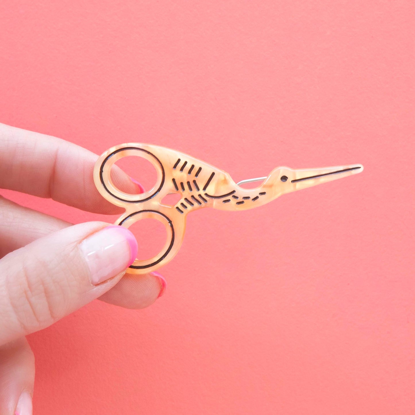 Model hand holding stork scissor hair barrette against a pink background.
