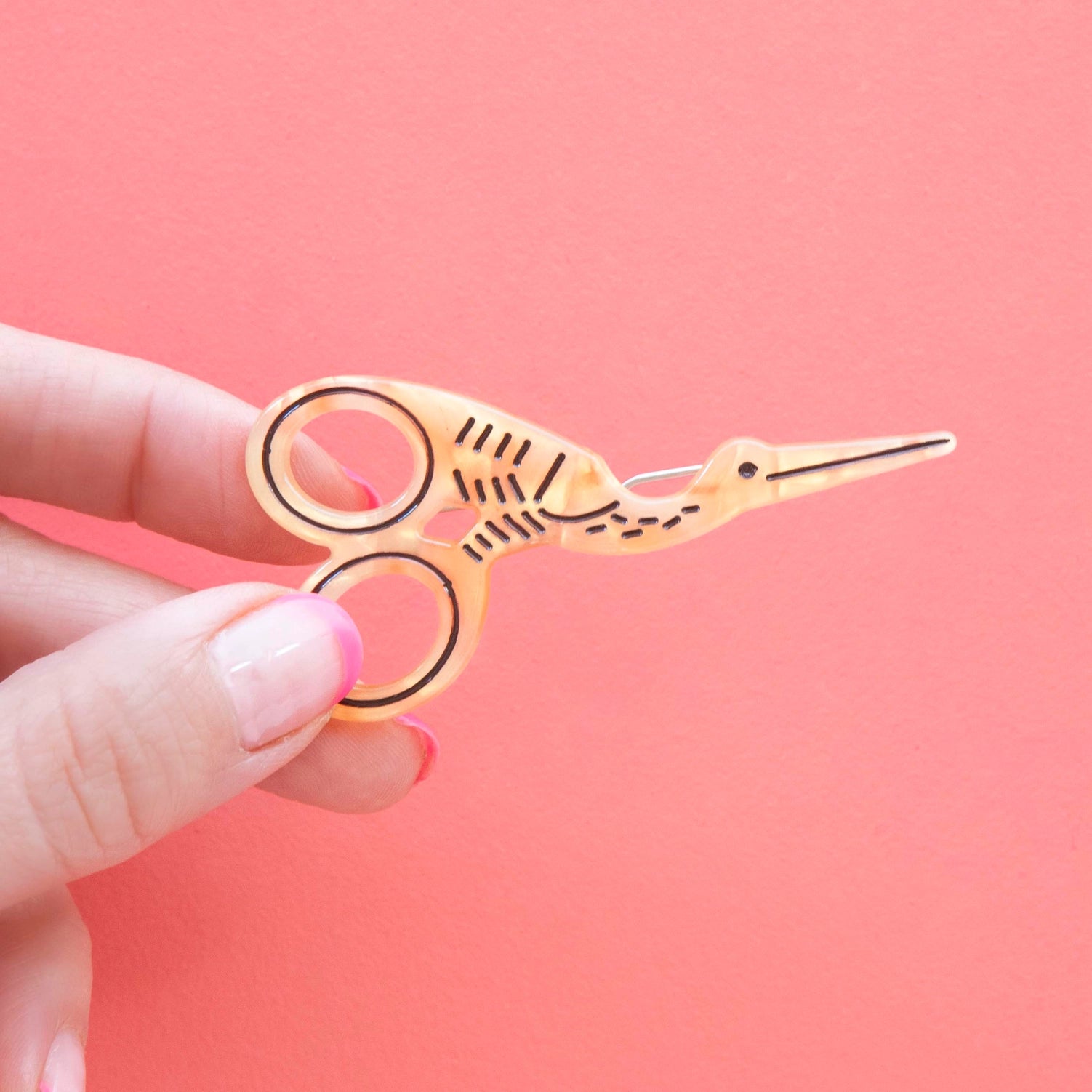 Model hand holding stork scissor hair barrette against a pink background.