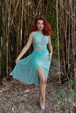 Model with bright red hair showcasing the front of the dress, while also showing the front fabric panel that moves against a bamboo forest background