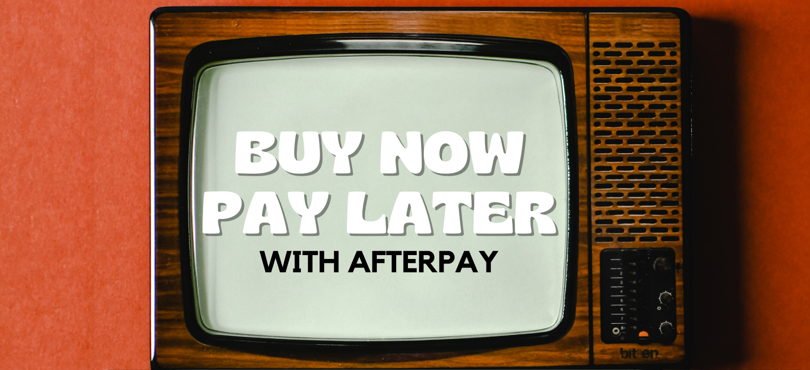 Vintage-style television screen with the words "BUY NOW PAY LATER WITH AFTERPAY" written on the screen. The background is wooden with an orange/red wall or backdrop, giving it a retro aesthetic.