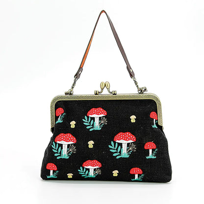 This photo shows the purse against a white background with the smaller strap shown. Purse is black with red topped mushrooms and smaller white mushrooms on it. Has a kisslock closure