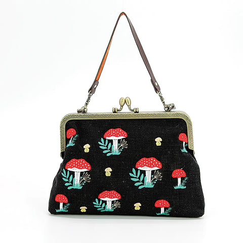 This photo shows the purse against a white background with the smaller strap shown. Purse is black with red topped mushrooms and smaller white mushrooms on it. Has a kisslock closure