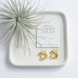 This photo showcases the Starburst earrings on a plate attached to their earring card with A Tea Leaf Jewelry's logo on it. The plate is also holding a succulent