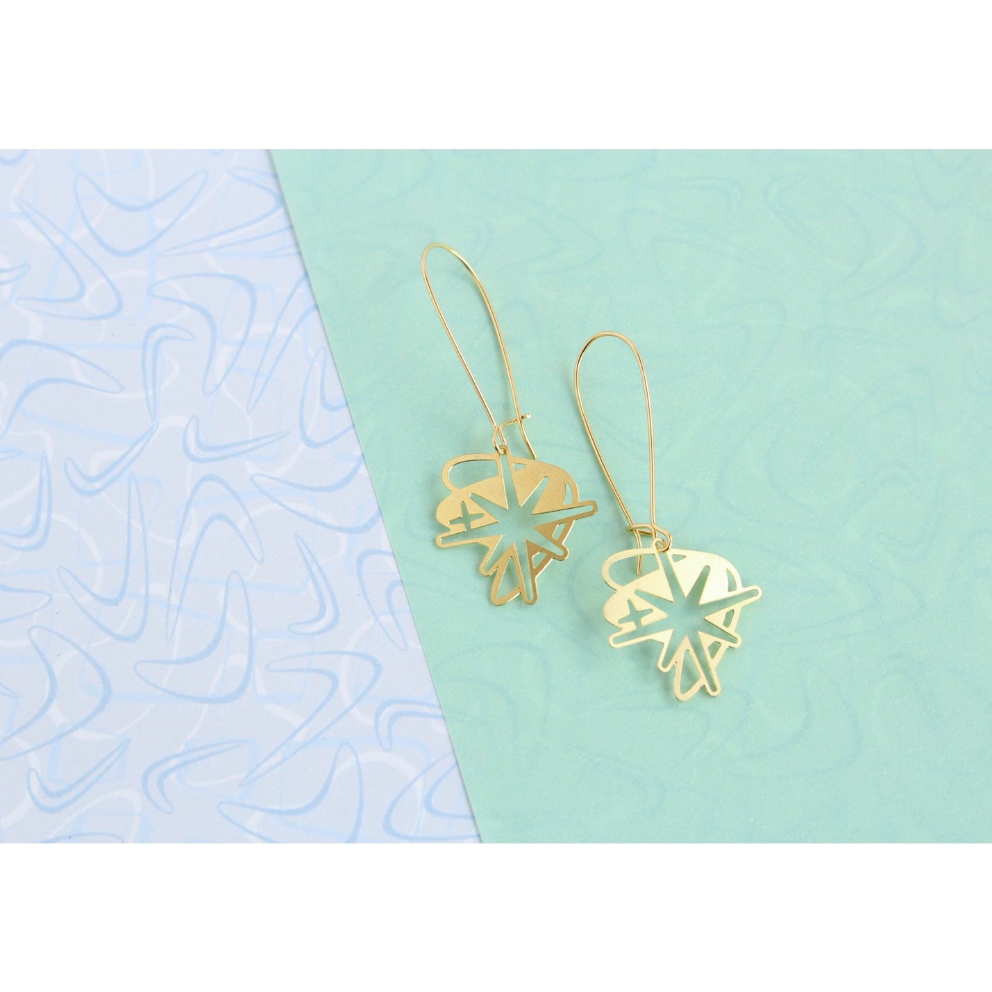 This photo showcase the earrings against a light blue background on one half, and an accent retro boomerang background to the left side of the background