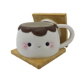 This photo shows the front of the mug. Mug is a large marshmallow with a kawaii face, chocolate on top of the marshmallow, and two graham crackers. Top graham cracker is the lid of the mug, and is shown in this photo as off of the mug to showcase that it is the lid.