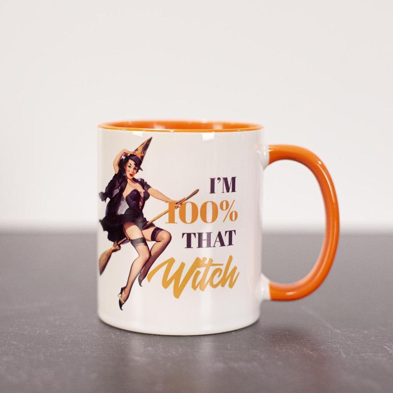 Witch pinup on broom. Orange and black lettering stating "I'm 100% that witch".