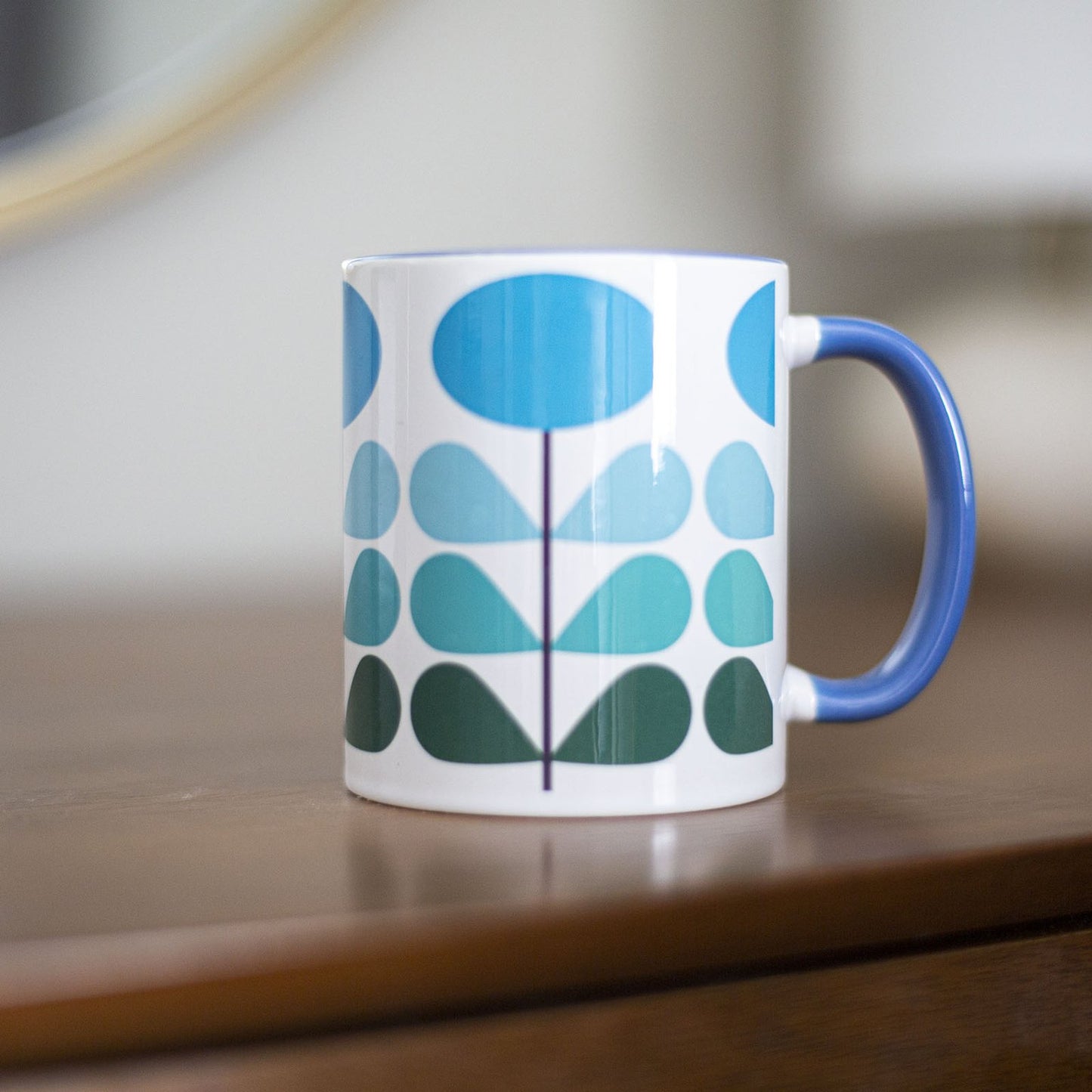 1950s mid century modern blue flowers on a white background coffee mug. Has ombre dark green to light blue leaves. Inside of mug is blue, and the handle is also dark blue.