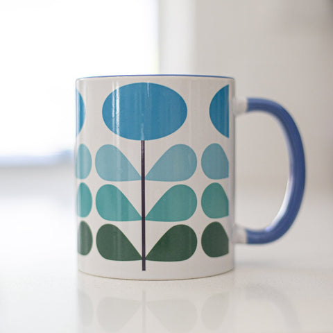 1950s mid century modern blue flowers on a white background coffee mug. Has ombre dark green to light blue leaves. Inside of mug is blue, and the handle is also dark blue.