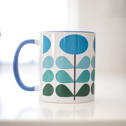 1950s mid century modern blue flowers on a white background coffee mug. Has ombre dark green to light blue leaves. Inside of mug is blue, and the handle is also dark blue.